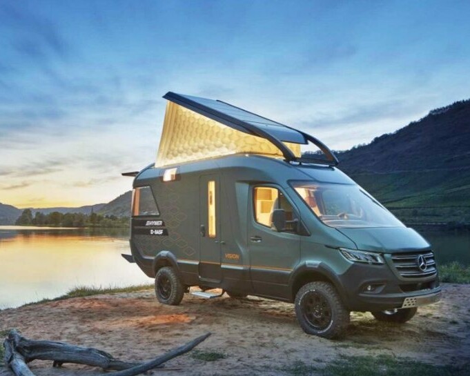 The Hymer VisionVenture campervan stands by a lake at dusk with the folding roof open.