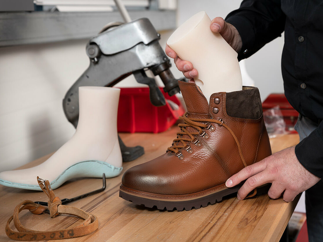 A countertop with a custom shoe last and the hands of a white man fitting a last into a brown leather orthopedic shoe.