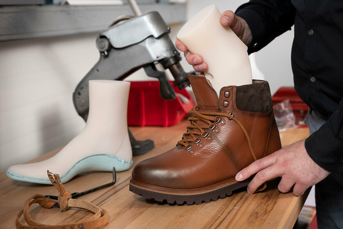 A countertop with a custom shoe last and the hands of a white man fitting a last into a brown leather orthopedic shoe.